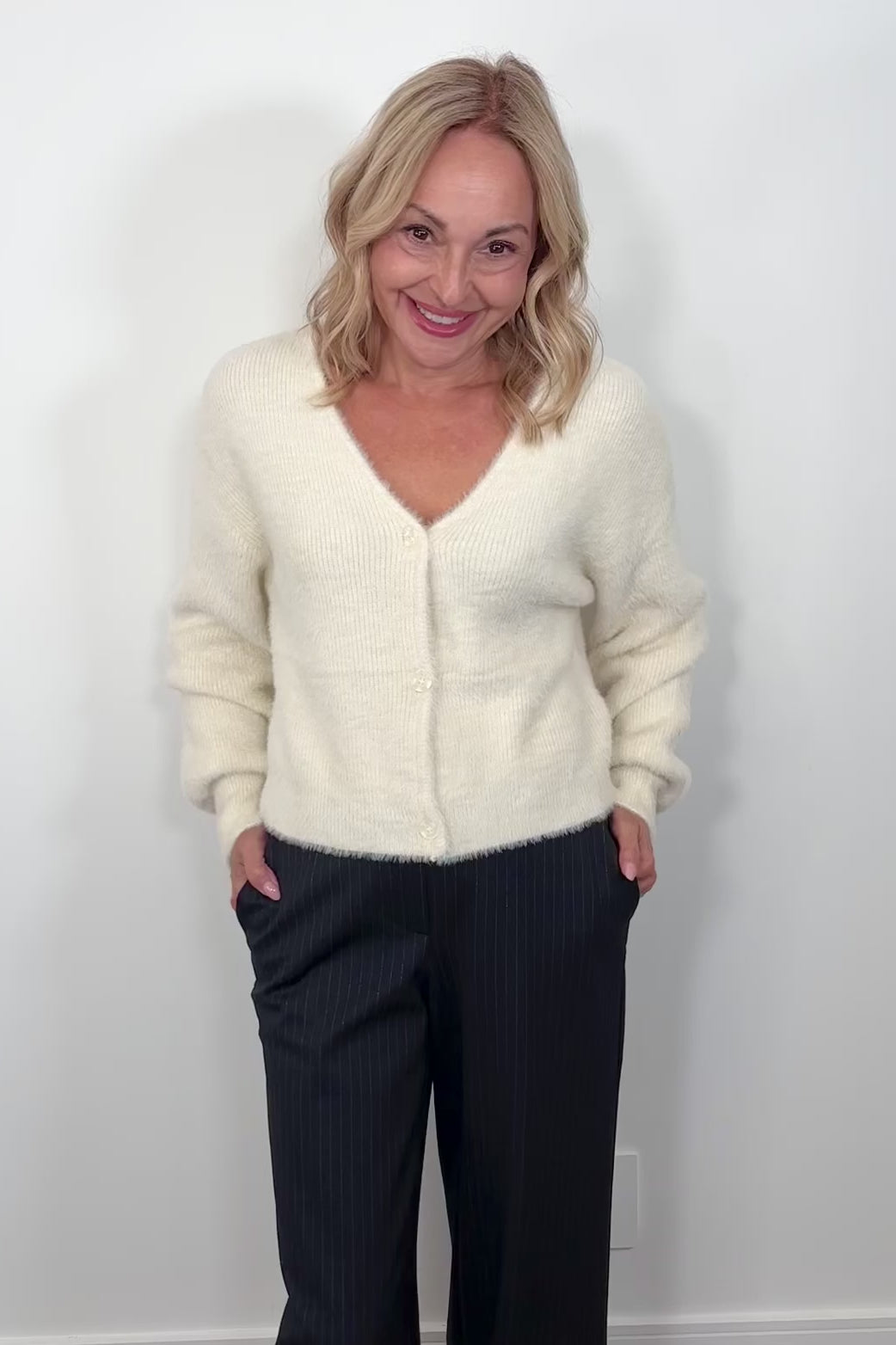 Video of a woman wearing a cream cardigan against a plain background