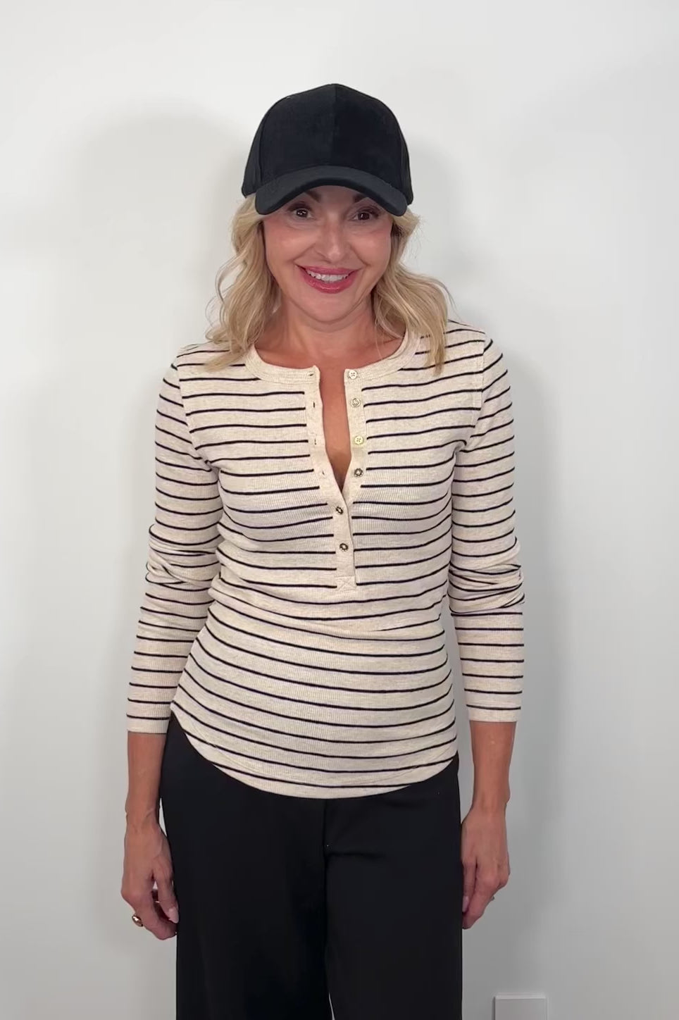 Video of a Woman wearing a striped henley shirt and black cap against a plain background