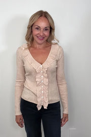 Video of a woman wearing an oatmeal coloured v-neck with ruffles long sleeve ribbed top turning to show the back of the garment.