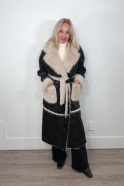 Video of a woman wearing an closed long black coat with fur detailing and hem on the collar, pockets and belt.