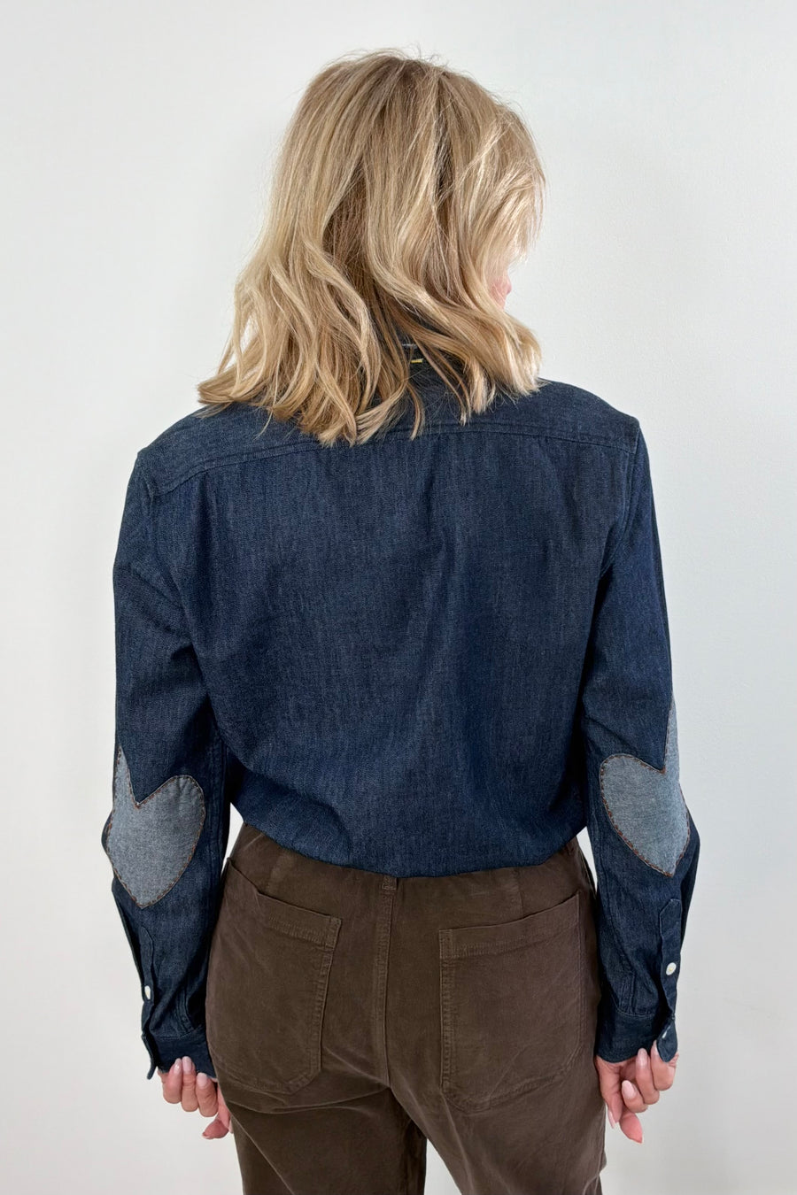 Woman wearing a blue denim shirt with brown heart patches on the elbow