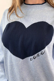 Close-up of a light blue sweater with a navy heart design and "XOXO" embroidered 
