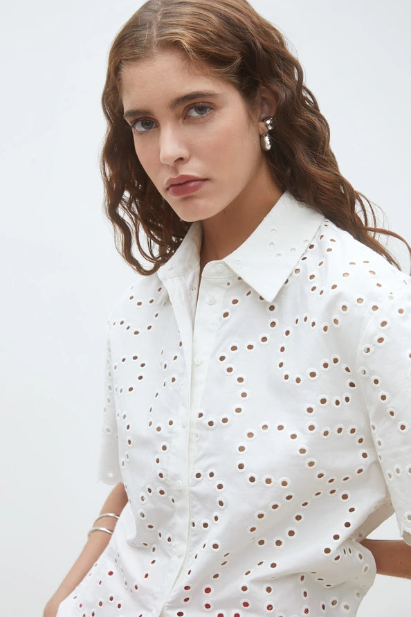 woman wearing a white short-sleeve eyelet blouse with a button-front design paired with red patterned shorts, detail