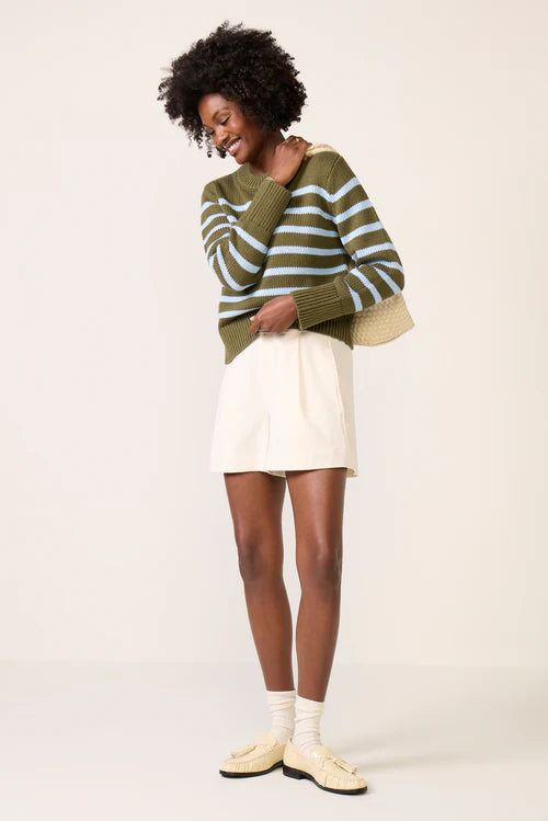 woman wearing a green cotton sweater with baby blue stripes with a white skirt and shoes
