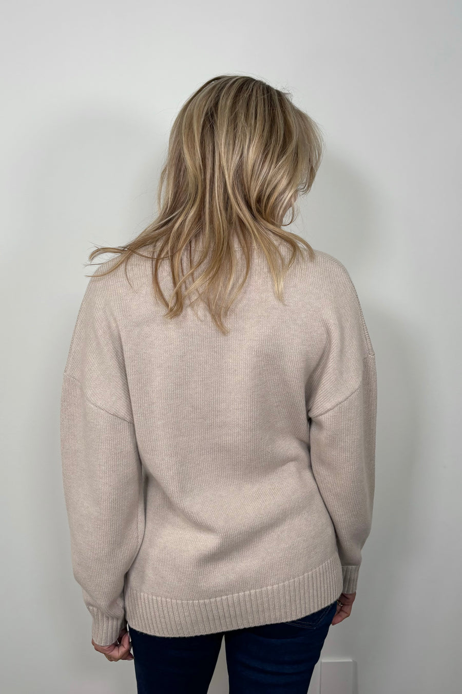 Back view of a woman wearing a fitted 3 button beige knitted cardigan