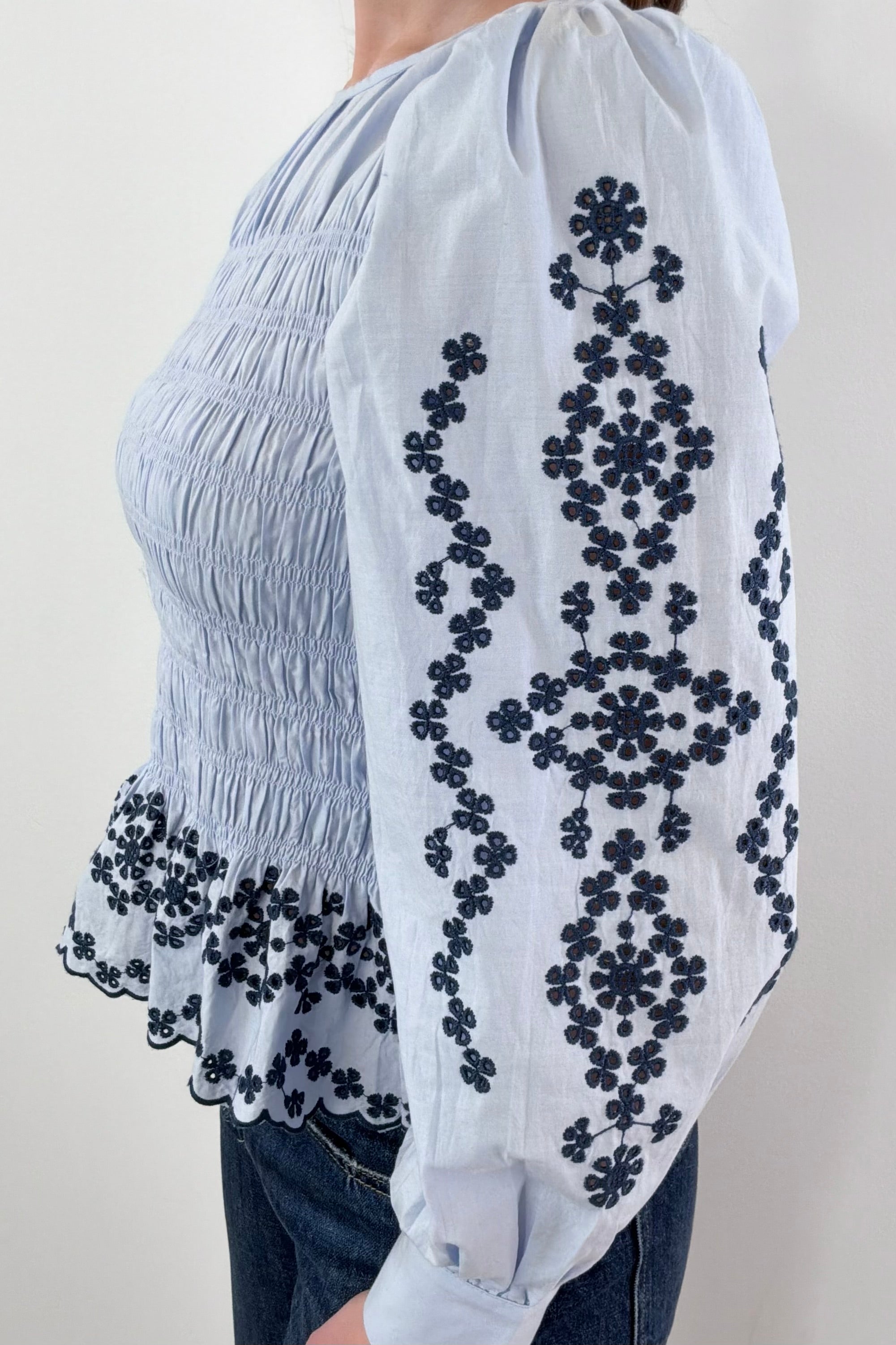 Side closeup of Woman wearing light blue smocked blouse with black detail