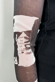 Front elbow zoom in view of woman wearing a black torso mesh-long sleeve top with prints on the sleeves