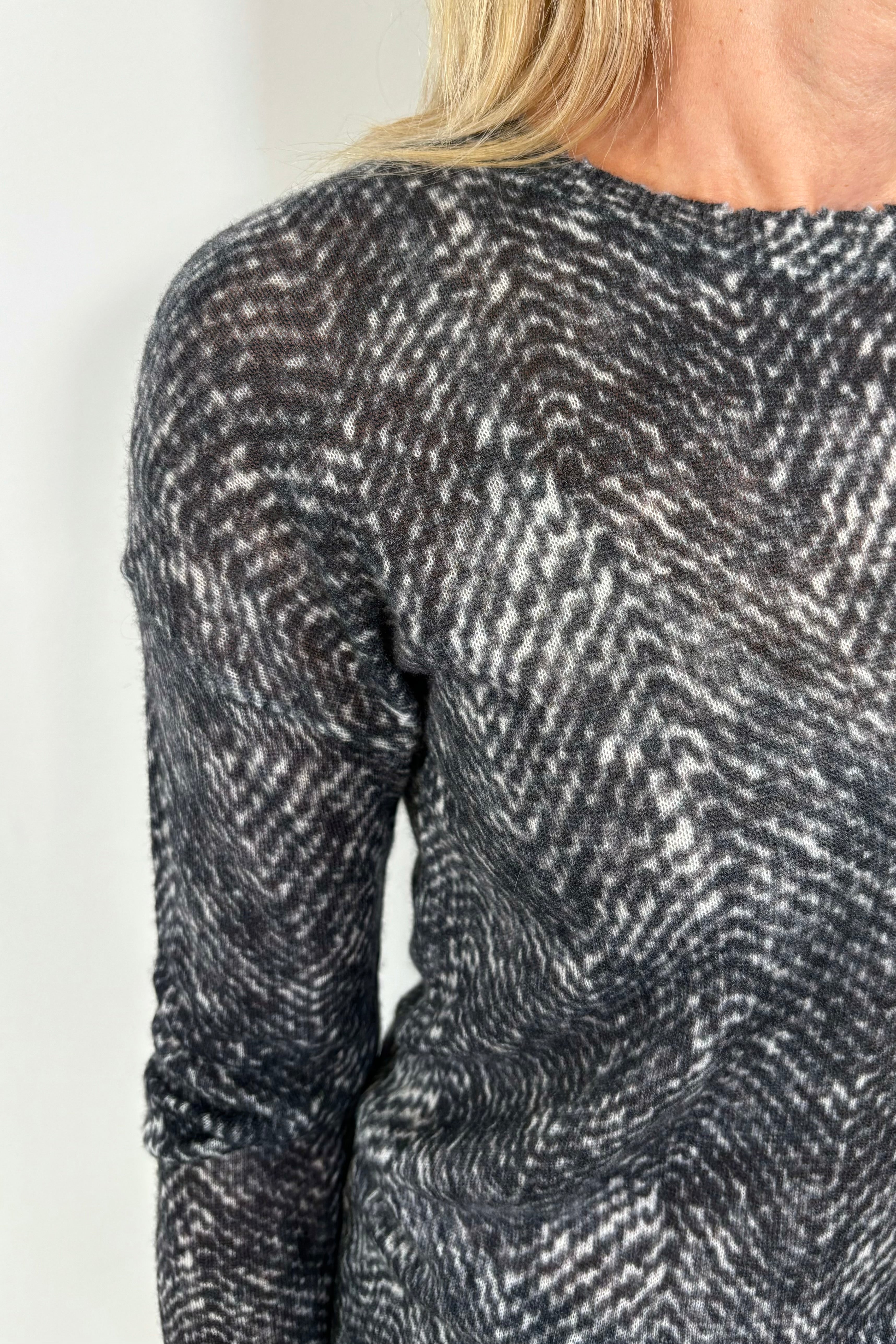 Zoom in of the shoulder of a woman showing a black and gray thin 100% cashmere long sleeve sweater.