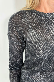 Zoom in of the shoulder of a woman showing a black and gray thin 100% cashmere long sleeve sweater.
