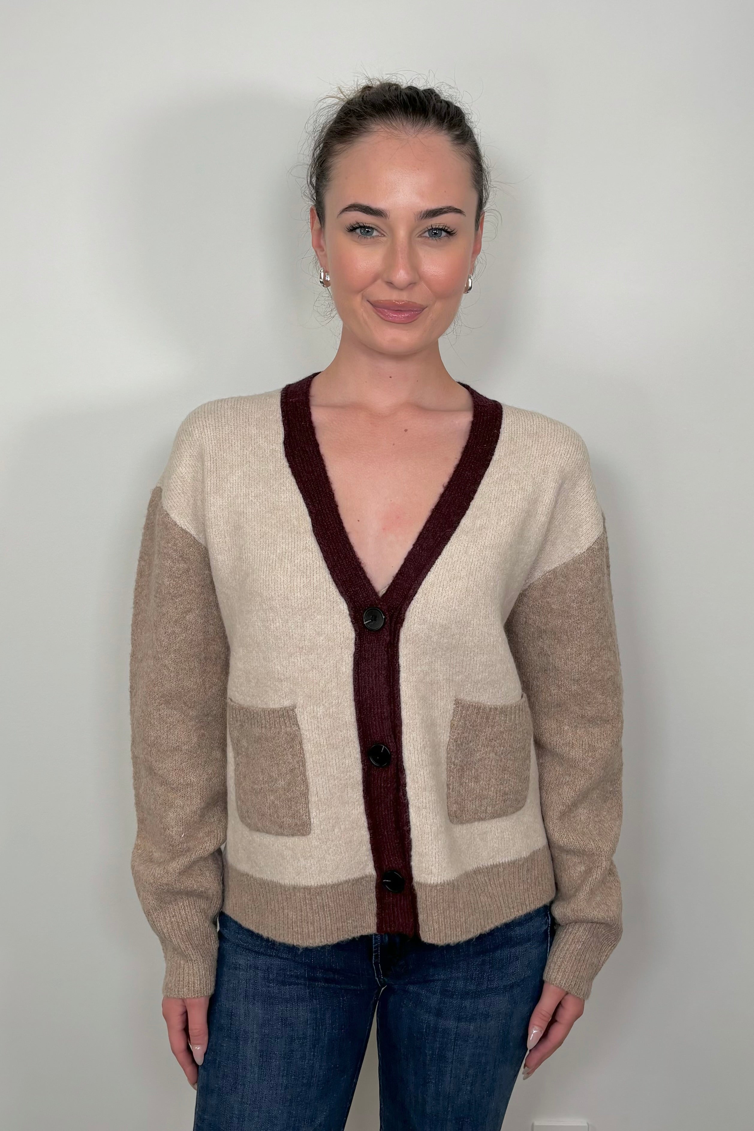 Front view of woman wearing a colour block beige and burgundy cardigan with pockets