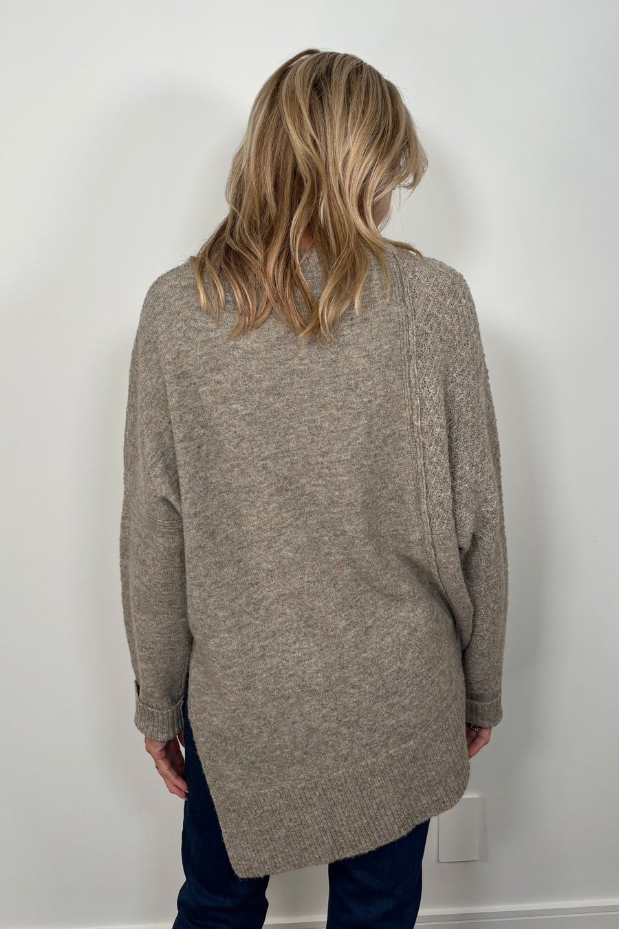 Back view of woman wearing a greige asymmetrical sweater 