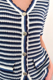 Close up of Woman wearing a navy, grey, white, black striped knit top with buttons