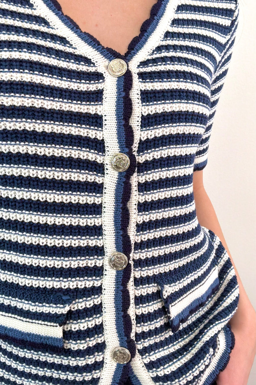 Close up of Woman wearing a navy, grey, white, black striped knit top with buttons