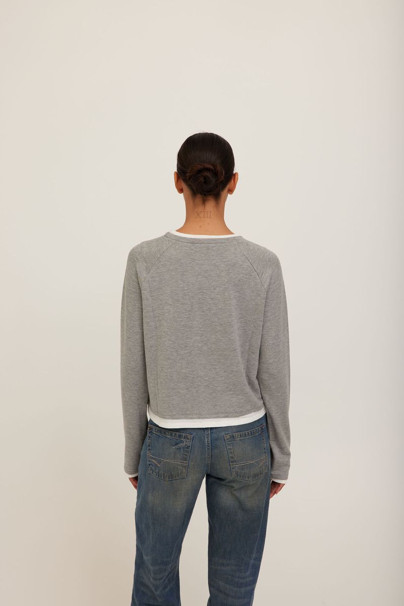 A model wearing a grey long-sleeve crewneck sweater with white ribbed trim at the collar, cuffs, and hem. 