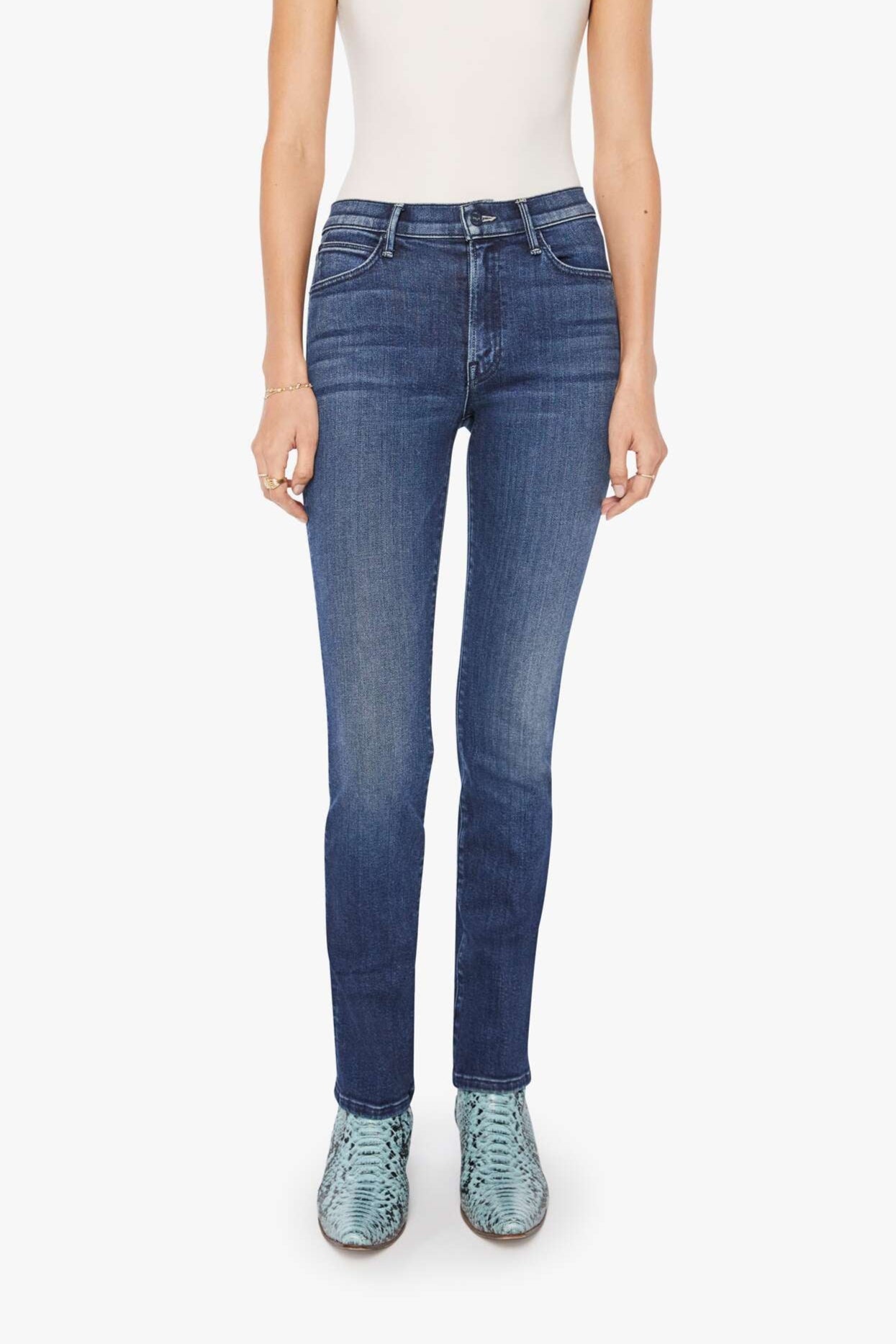 Woman wearing a white tank top and blue mid-rise, straight leg jeans on a white background