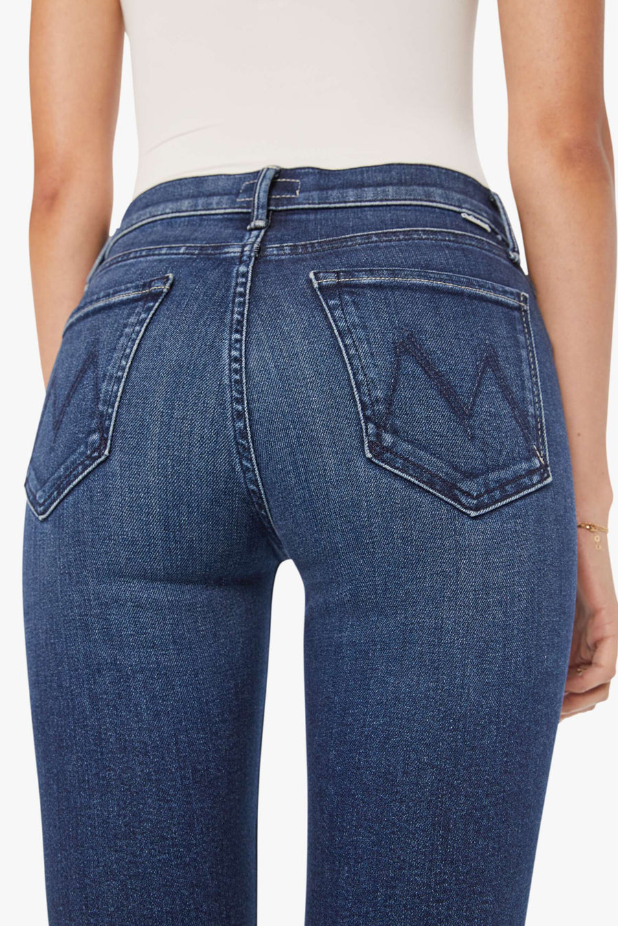 Woman wearing a white tank top and blue mid-rise, straight leg jeans on a white background zoom in from the back