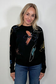 Front view of woman wearing a knit black top with all over coloured detailing
