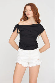 Woman wearing a black off-shoulder top and white shorts on a plain background