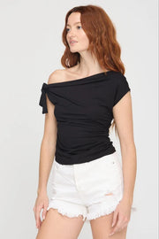 Woman wearing a black off-shoulder top and white shorts on a plain background