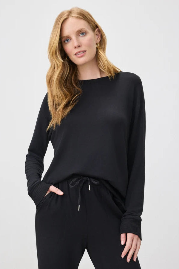 A woman modeling a black long-sleeve knit top with matching black drawstring sweatpants against a light gray studio background.