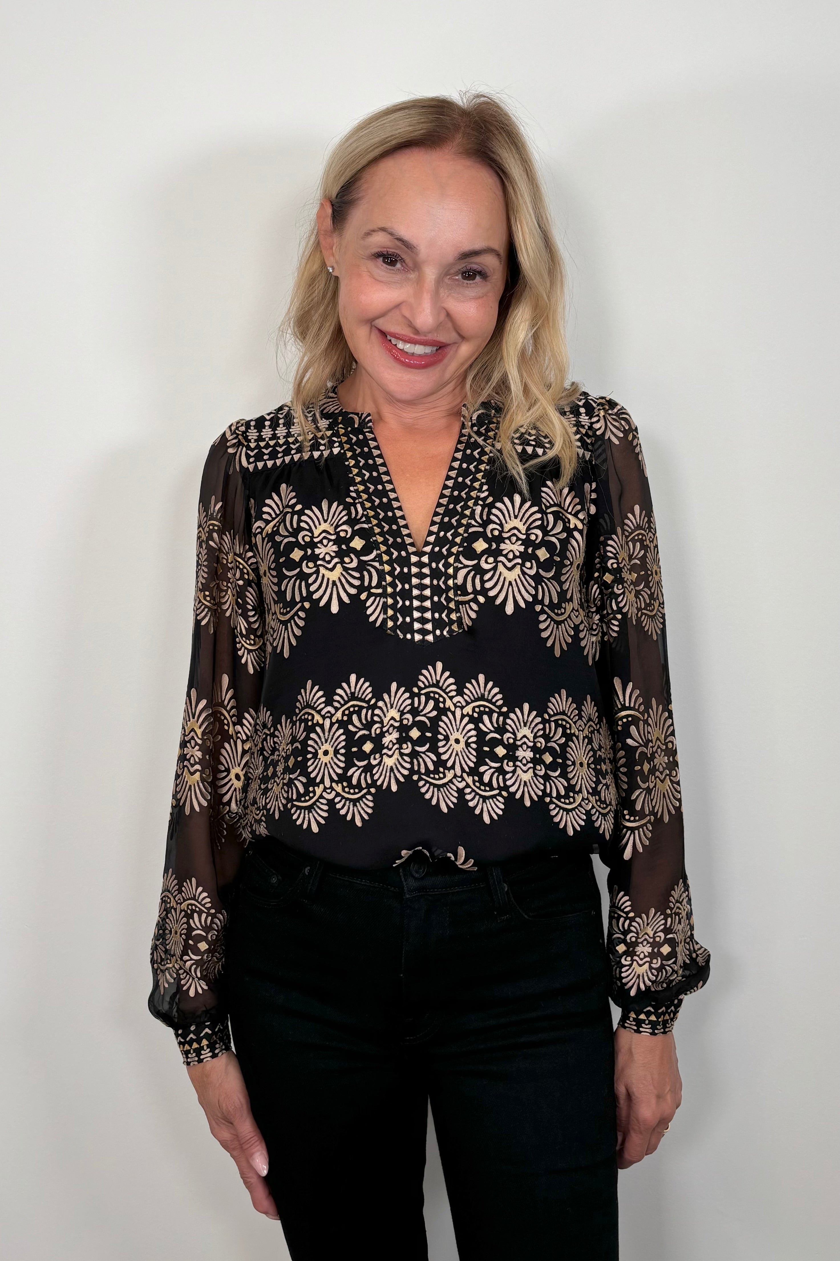 Front view of woman wearing a silk mix black and gold long sleeve burnout blouse tucked in