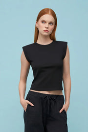Woman wearing a black sleeveless top and black pants against a light blue background