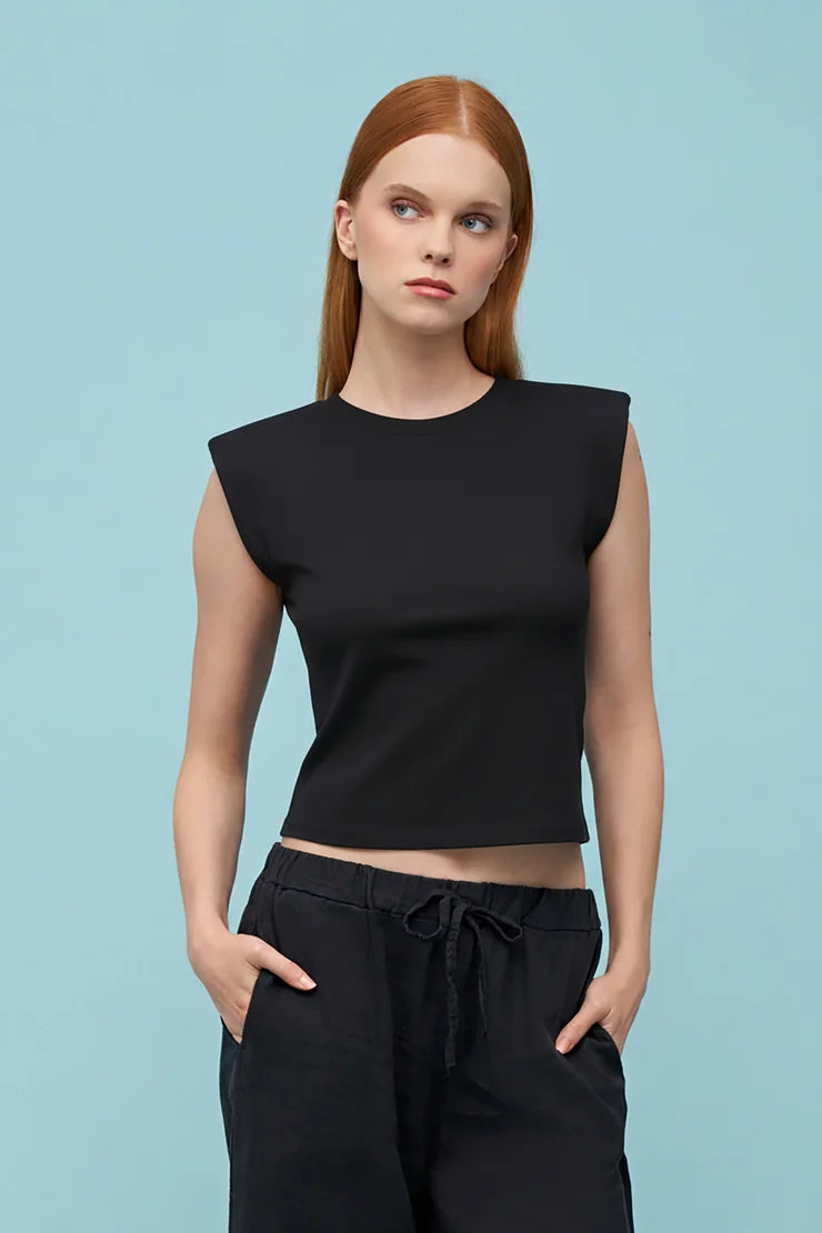 Woman wearing a black sleeveless top and black pants against a light blue background