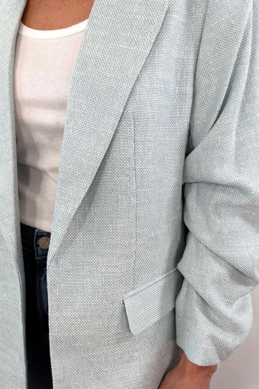 Close up of a light turqoise open blazer with rouched sleeves