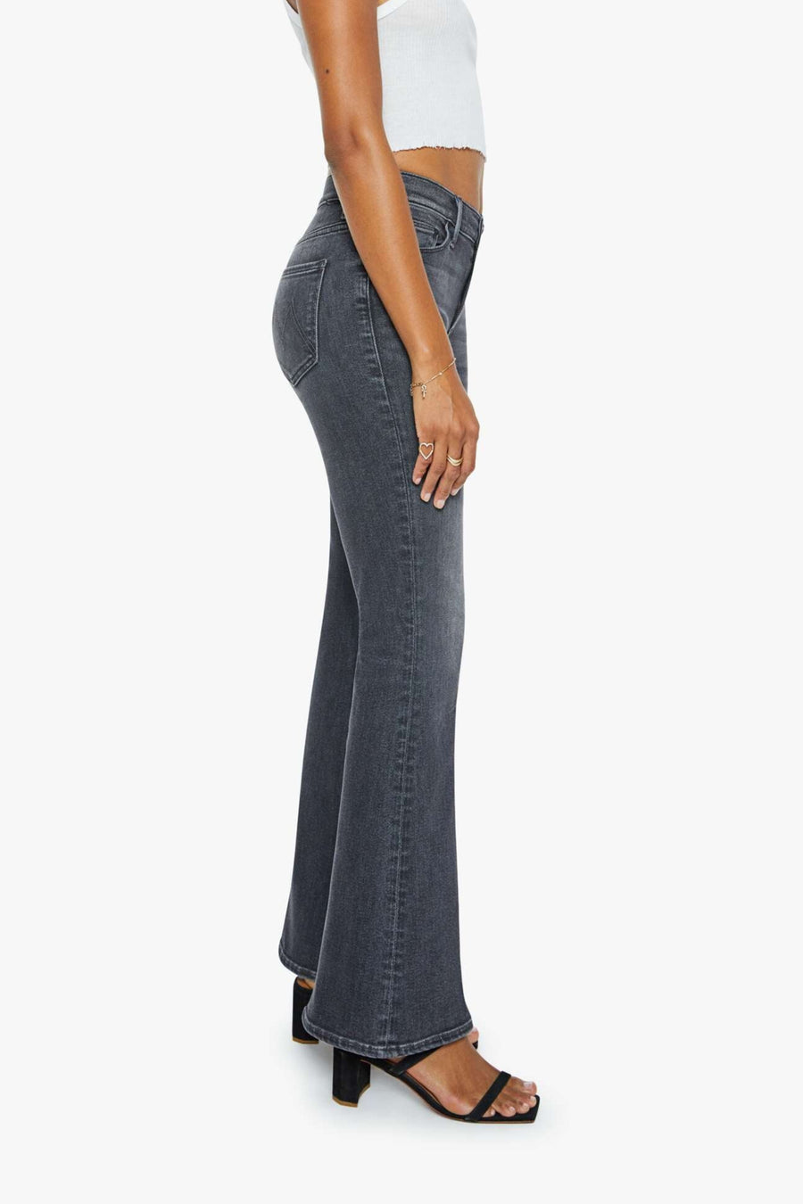 Woman wearing a white tank top and washed black mid-rise, soft flare jeans on a white background. Side view