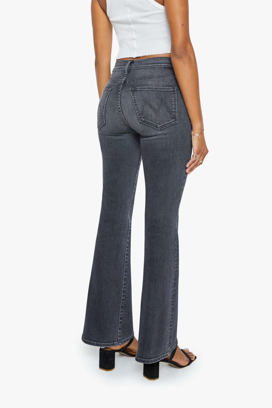 Woman wearing a white tank top and washed black mid-rise, soft flare jeans on a white background. Back view