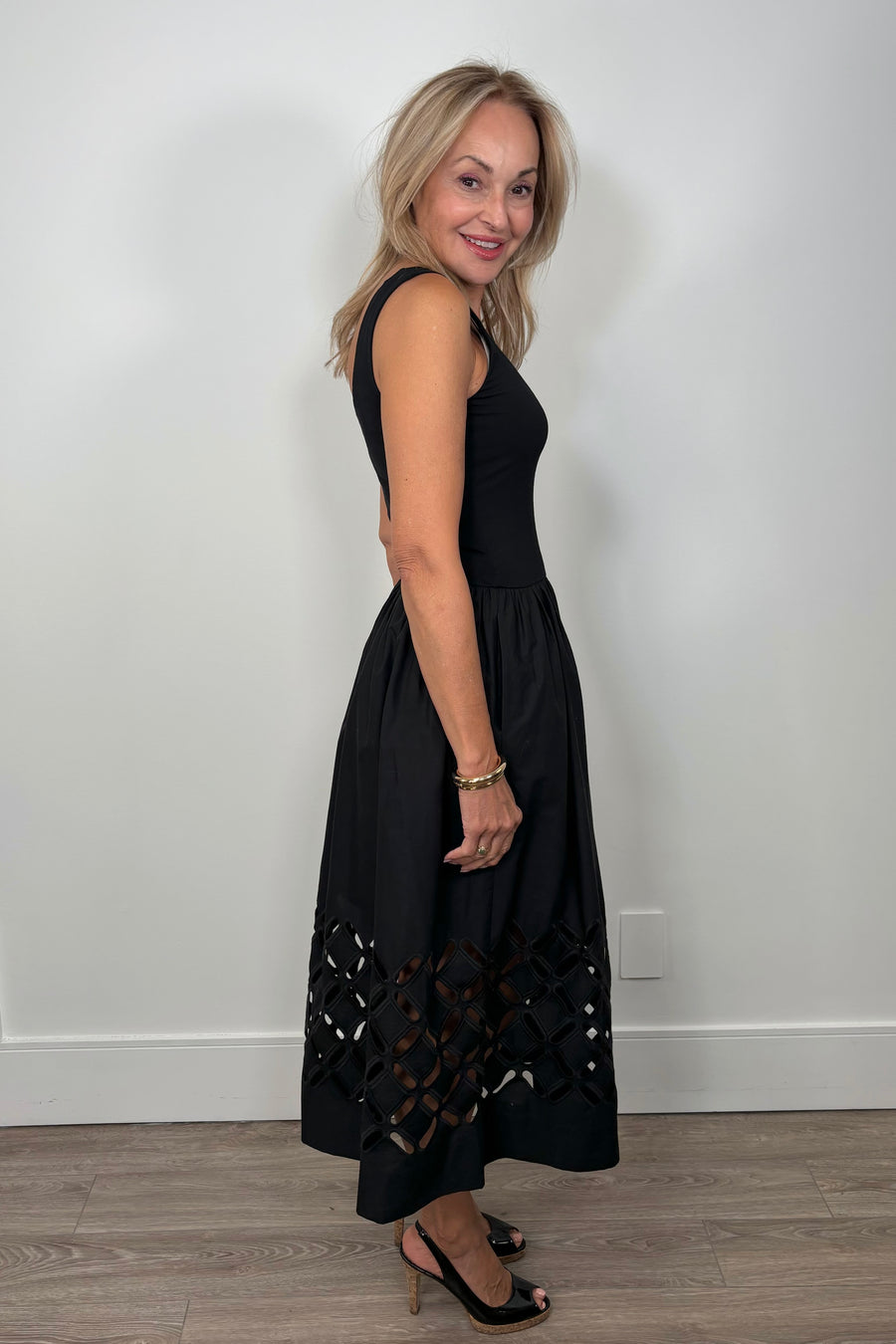 Side view of a woman wearing a black cotton dress with cut outs in the bottom