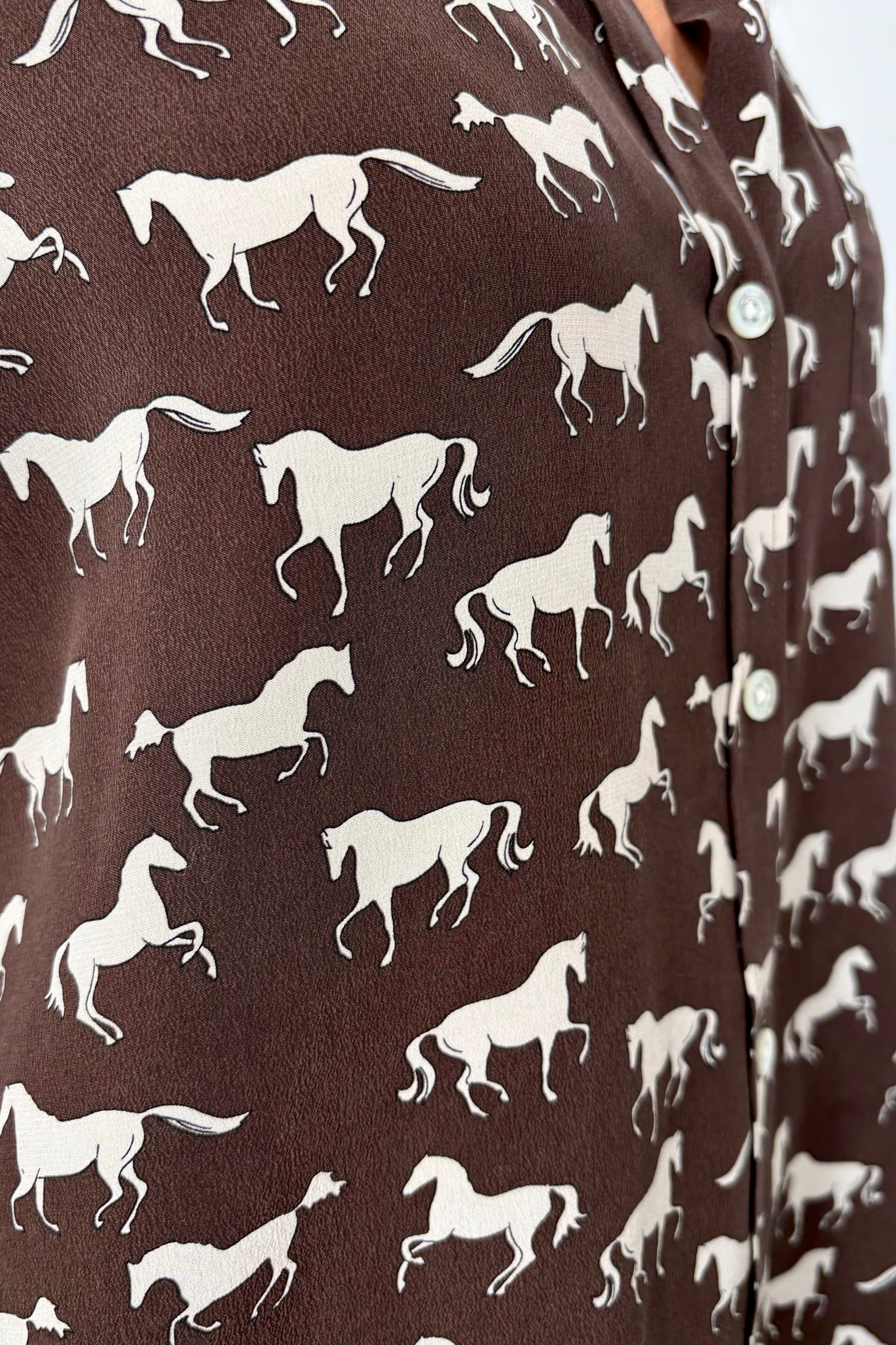Close-up of a brown silk blouse with a white horse pattern all over 