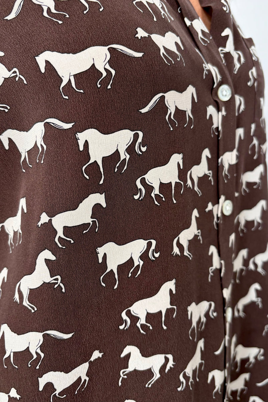 Close-up of a brown silk blouse with a white horse pattern all over 
