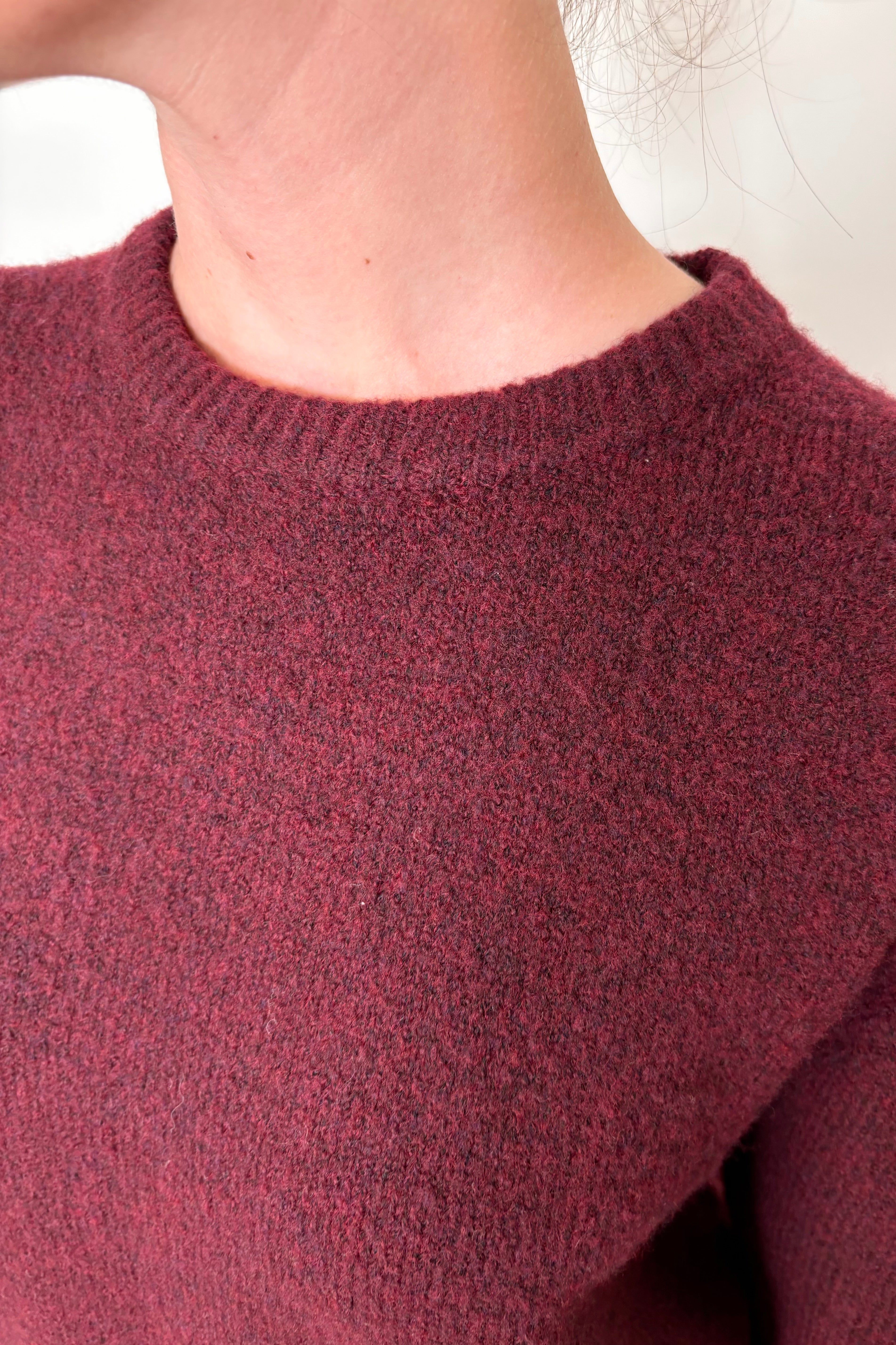 Close-up view of woman wearing a wine coloured crew-neck sweater 
