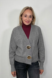 Front view of woman wearing a gray cardigan with silver looking hardwear with a wine coloured turtleneck knitted top