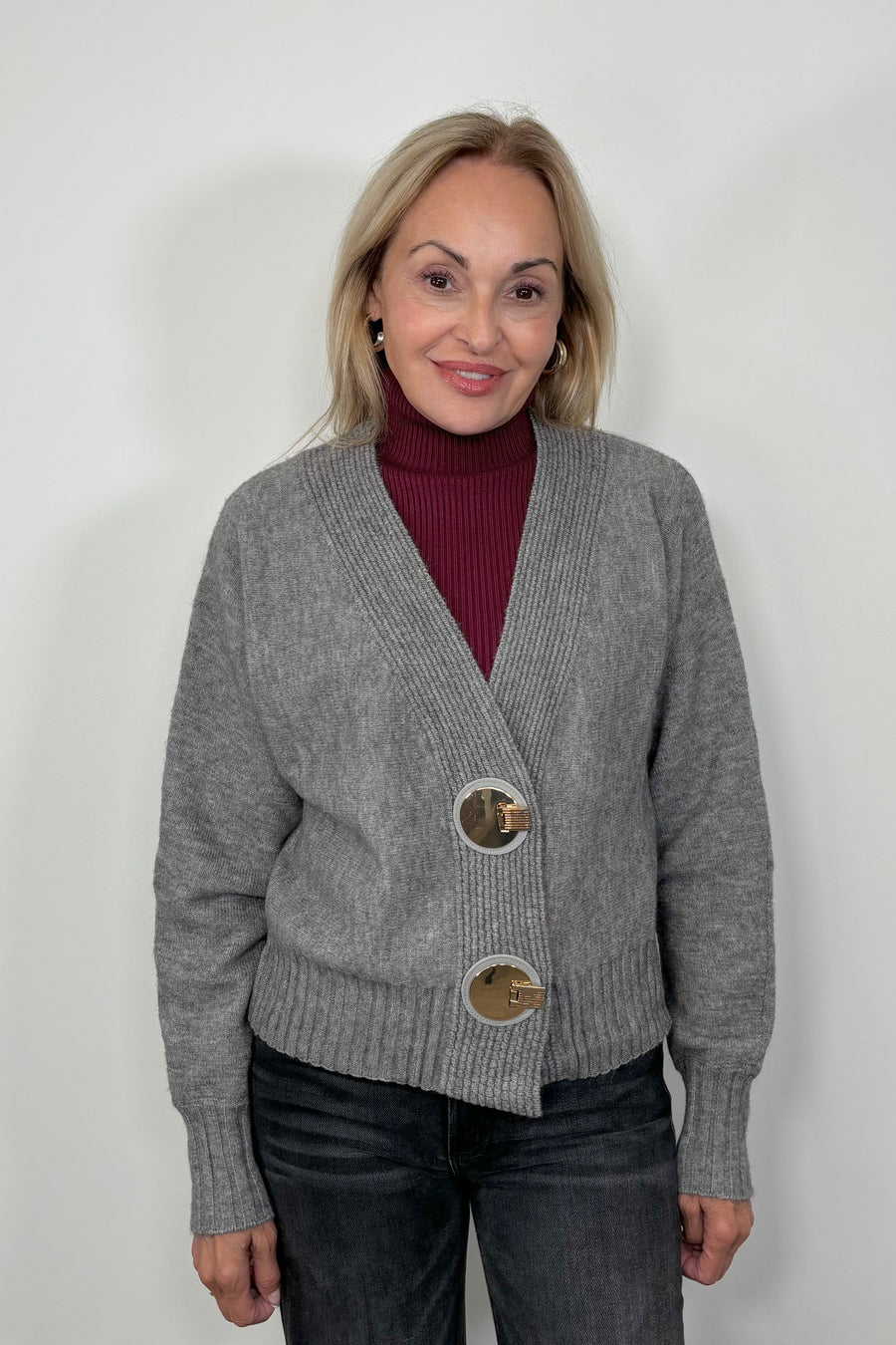 Front view of woman wearing a gray cardigan with silver looking hardwear with a wine coloured turtleneck knitted top