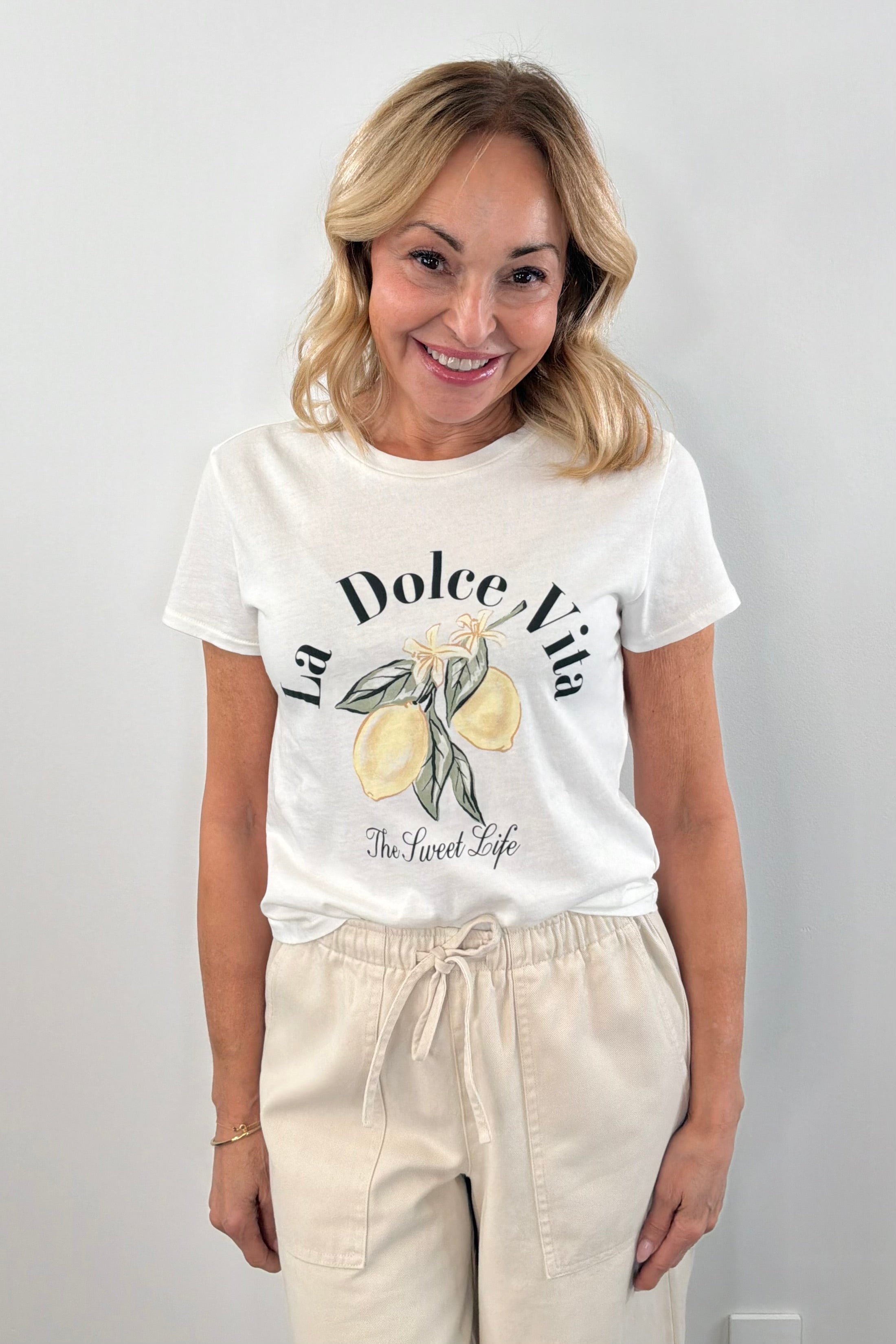 Woman wearing a white short sleeve graphic tee with the words "La Dolce Vita The Sweet Life" on the front and a picture of lemons
