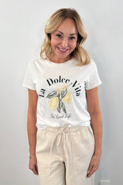 Woman wearing a white short sleeve graphic tee with the words "La Dolce Vita The Sweet Life" on the front and a picture of lemons