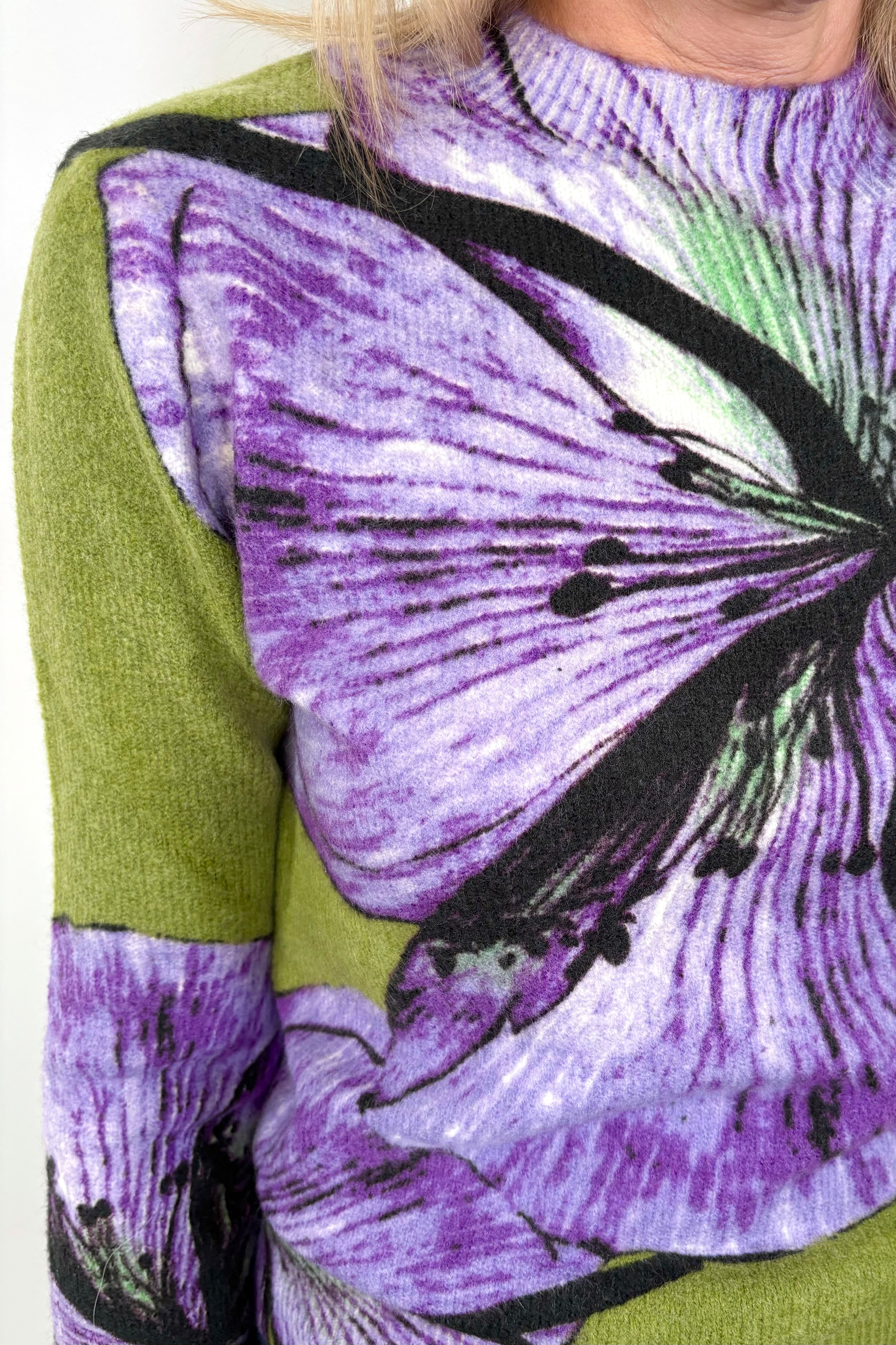 Front view shoulder zoom in of woman wearing a green sweater with purple orchids all over