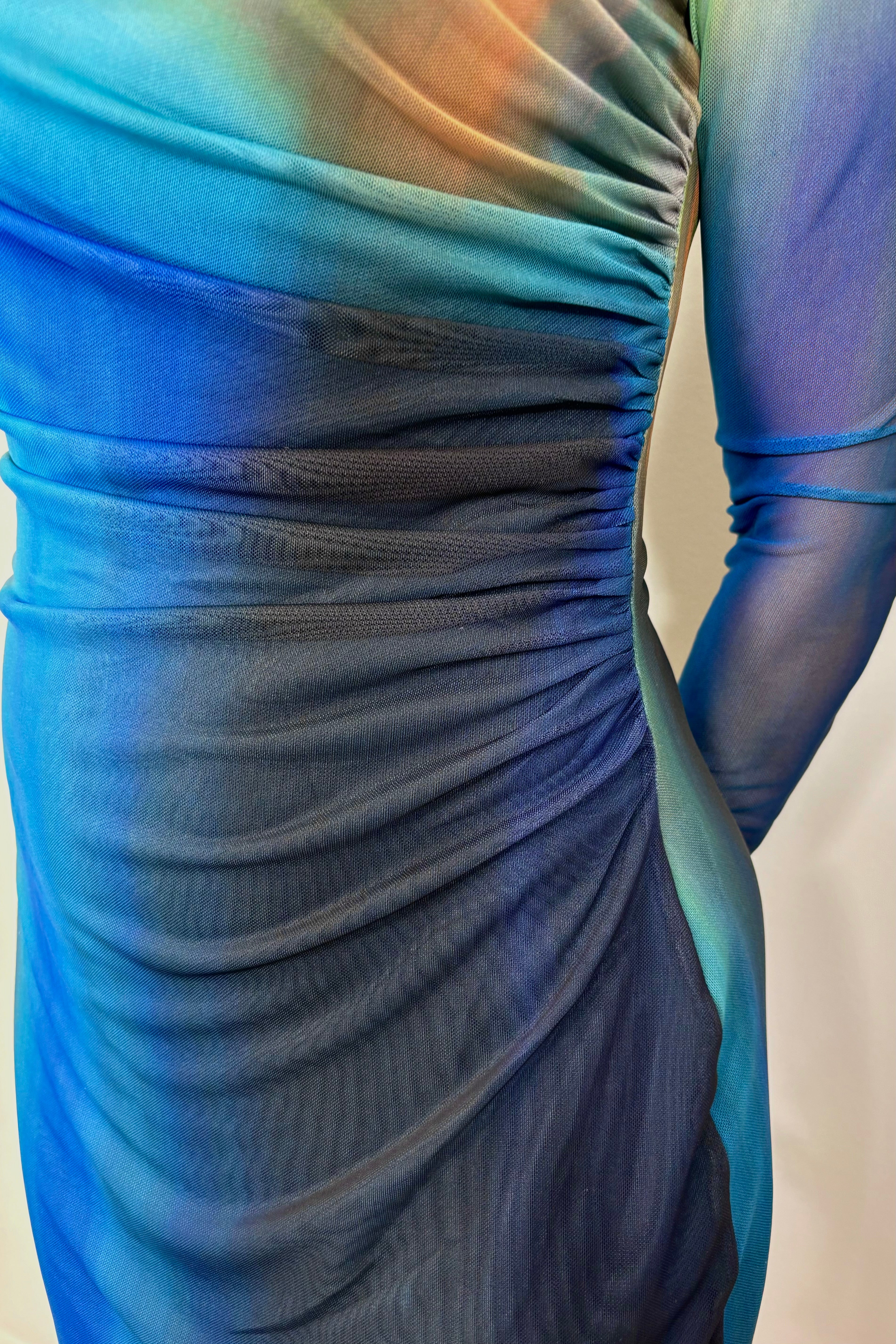 Zoom in of woman wearing a blue and green dress with sheer sleeves on a white background