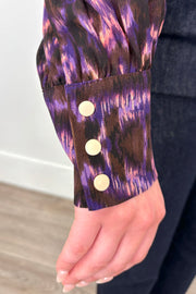 Close up of the cuff of a violet sheer printed blouse with ruffles tucked in