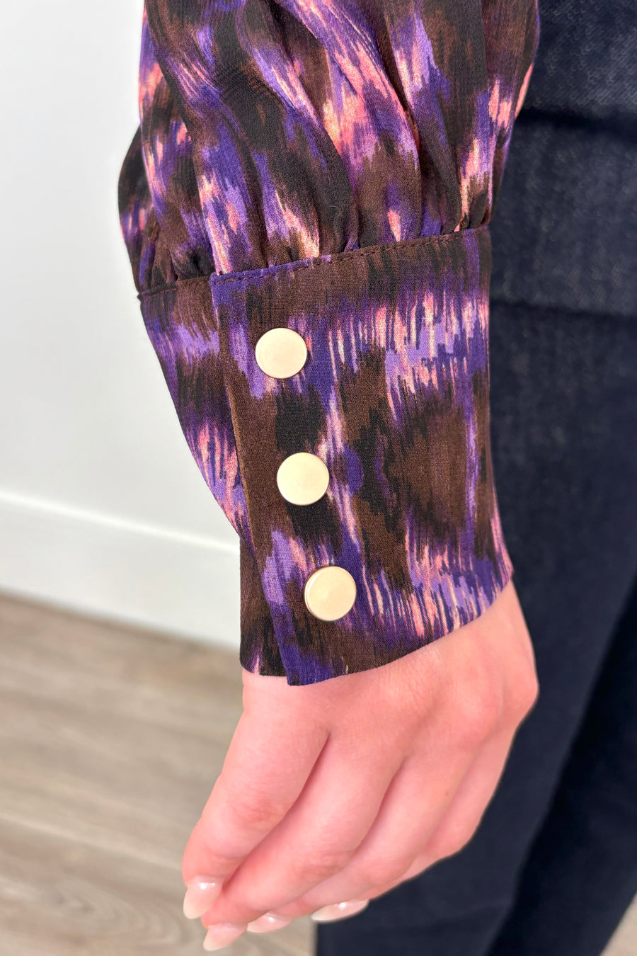 Close up of the cuff of a violet sheer printed blouse with ruffles tucked in