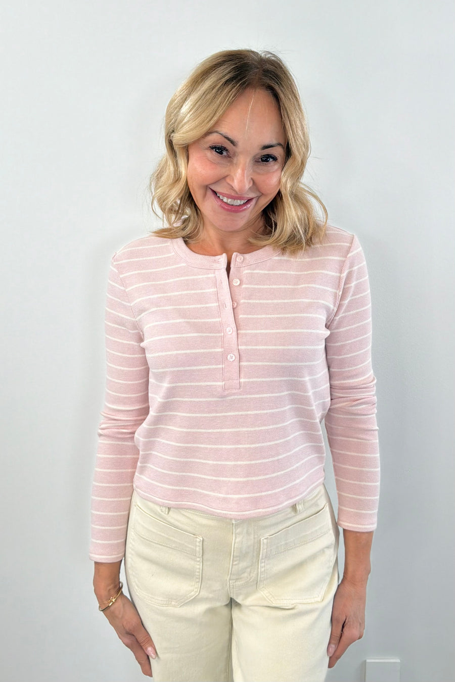 Woman wearing a long sleeved pink henley knit top with cream stripes and a button placket