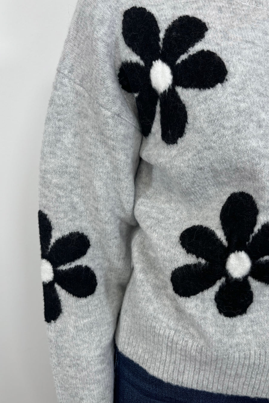 Zoom in view of woman’s shoulder wearing a gray cardigan with a black daisy pattern and buttons, done up