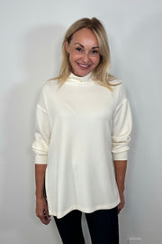 Front facing woman wearing a white boxy turtleneck top