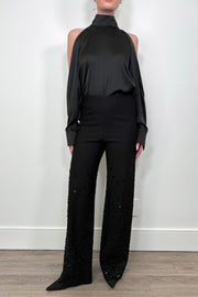 Person wearing a black outfit with a high-neck top and wide-leg pants against a white wall.