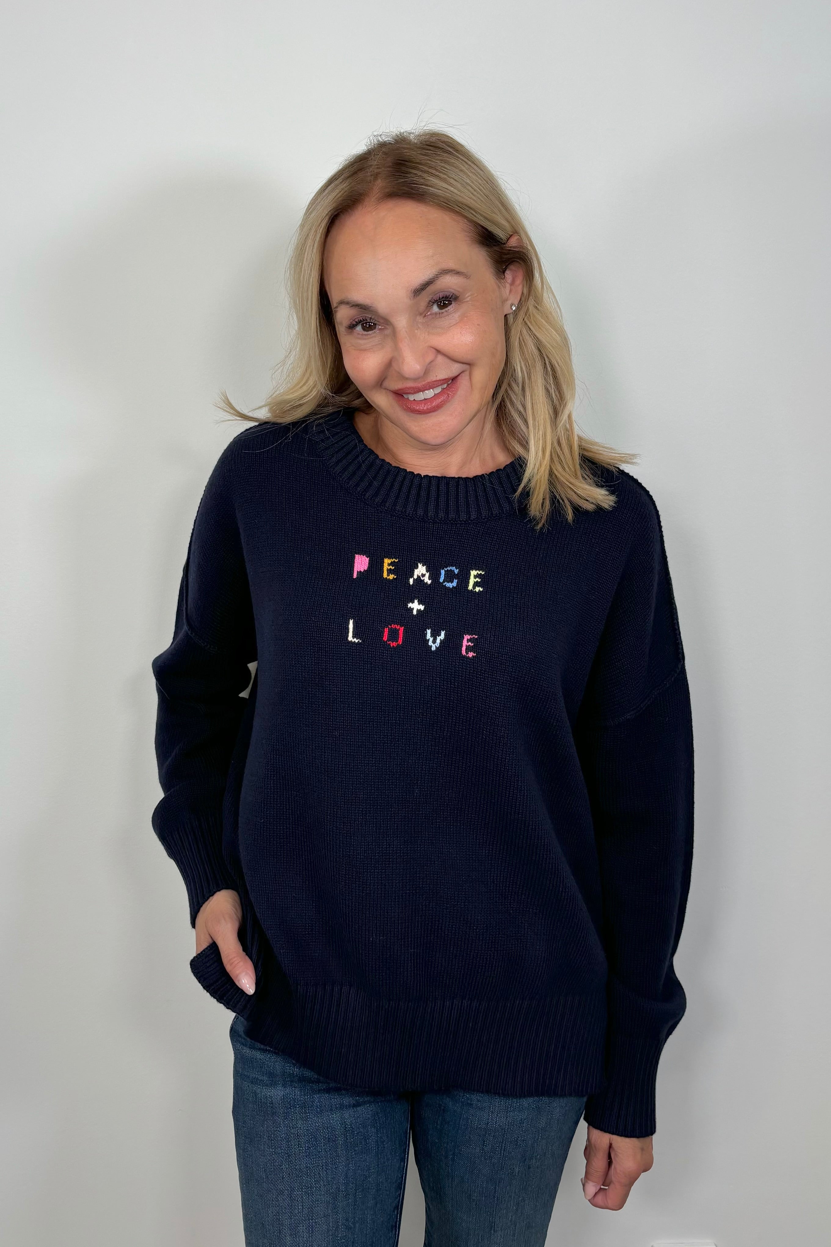 Woman wearing a navy blue sweater with “Peace & Love” embroided