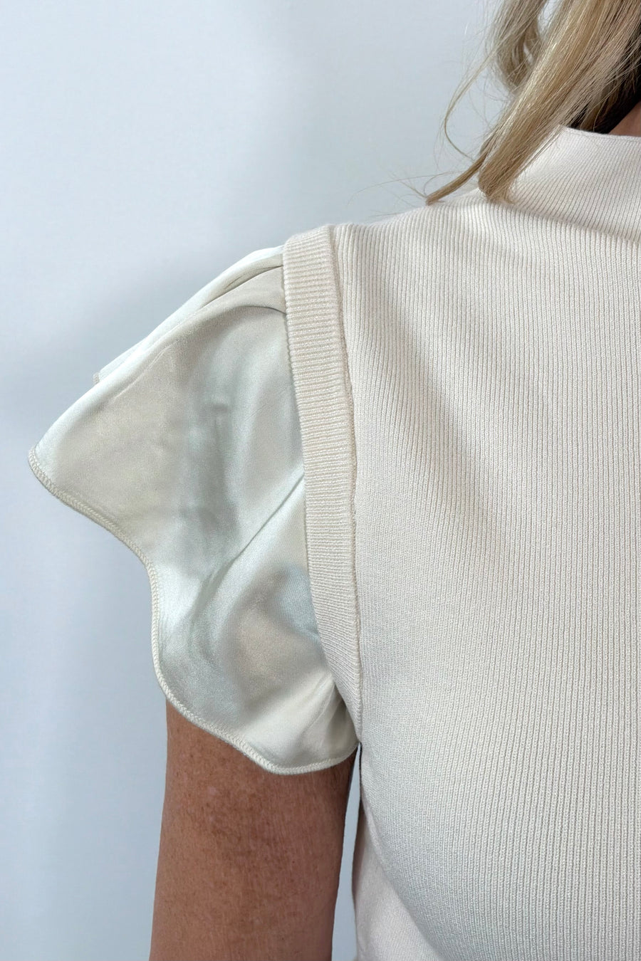 Close-up of a person wearing a beige sleeveless top with satin ruffles against a light background