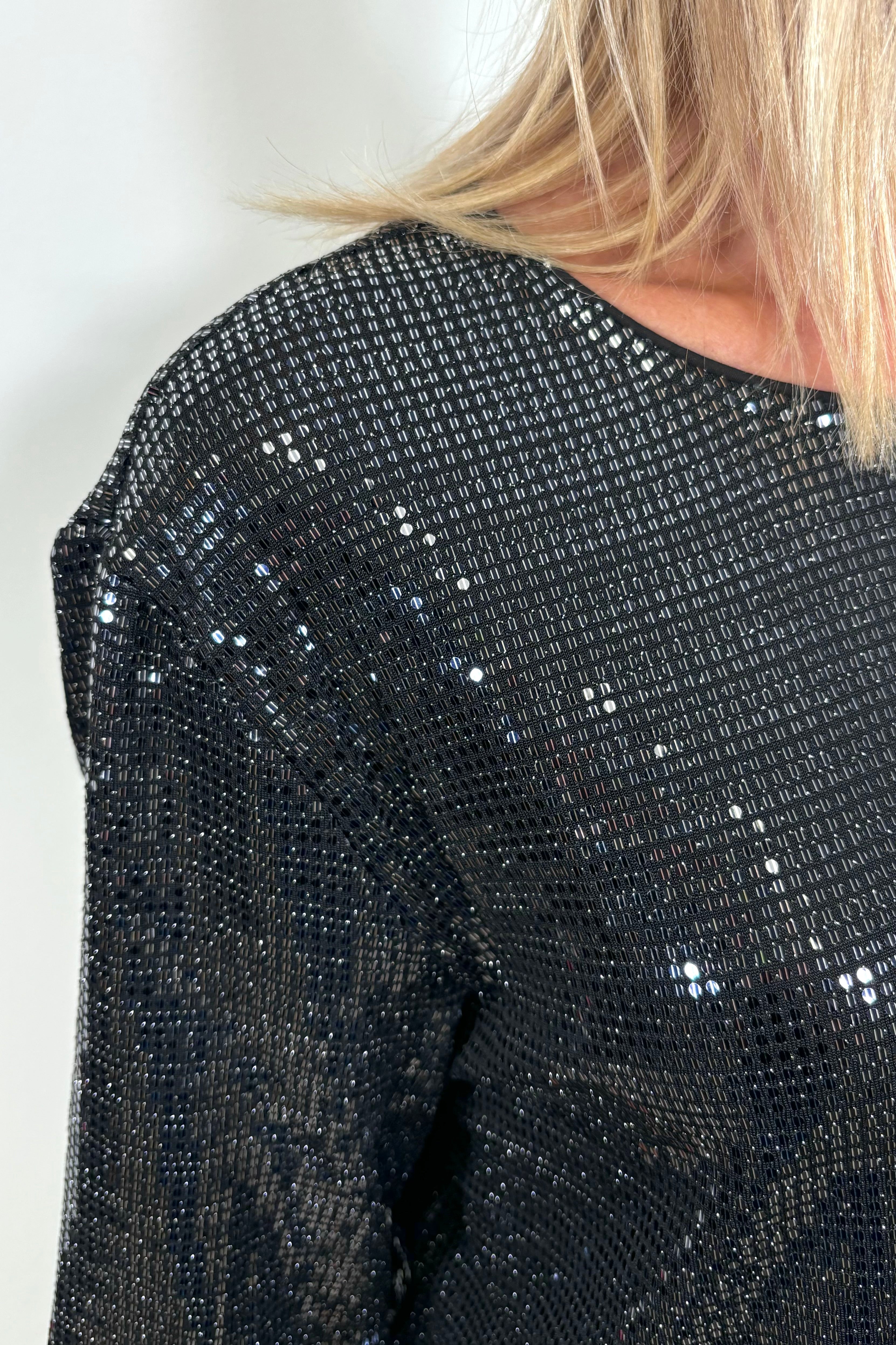 Zoom in of the right shoulder of a woman wearing a shimmery crew top
