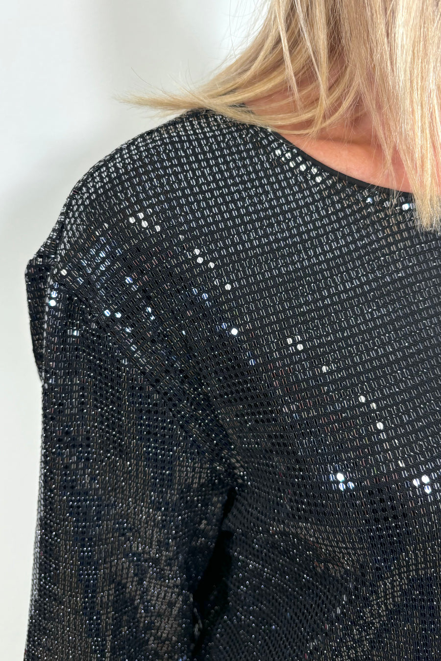 Zoom in of the right shoulder of a woman wearing a shimmery crew top